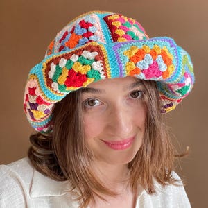 May include: A colorful, handmade crochet bucket hat. The hat features a patchwork design with squares in various colors including red, orange, blue, and green. The brim is a solid light blue. A unique, vibrant accessory.