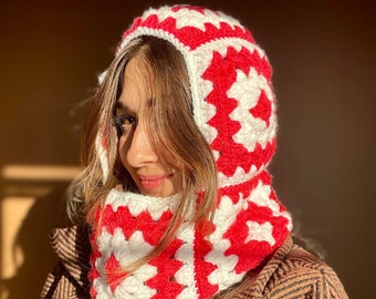 May include: A red and white crocheted hooded scarf with a square pattern. The scarf is worn by a person with brown hair.