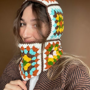 May include: A brown, white, blue, orange, and green crocheted hooded scarf with a geometric pattern.