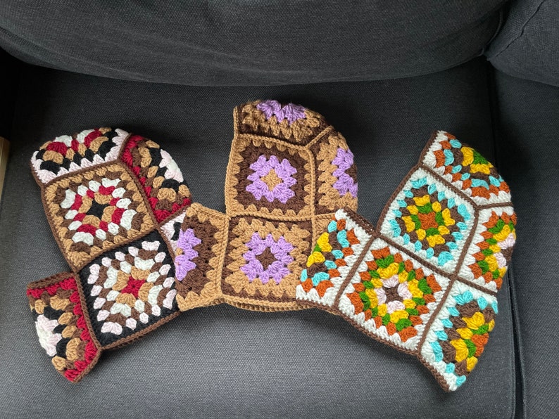 May include: Three crocheted granny squares in different colors and patterns. The squares are brown, purple, and blue with white and yellow accents. The squares are joined together to form a larger piece.