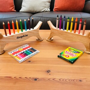 May include: Two wooden dachshund pencil holders, one with the name "Sophie" engraved on it. The holders are filled with coloured pencils and crayons.