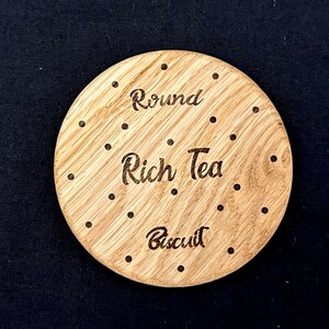 May include: A round wooden coaster with the words "Round Rich Tea Biscuit" engraved on it. The coaster has a brown wood grain and is decorated with small dots.