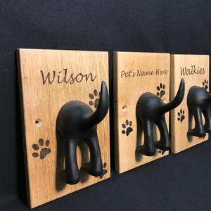 May include: Three wooden dog lead hooks with black dog tail hooks. The hooks are engraved with the names "Wilson", "Pet's Name Here", and "Walkies".