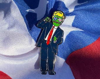 May include: A green frog wearing a blue suit, red tie, and sunglasses with an American flag design. The frog has a blonde wig and is holding a microphone. The frog is standing on a red, white, and blue American flag.