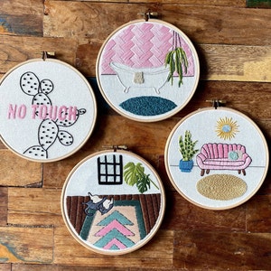May include: Four embroidered hoops featuring different designs. The first hoop has a pink and white design with a bathtub and the text "No Touch". The second hoop has a pink and white design with a sofa and a plant. The third hoop has a green and white design with a window and a plant. The fourth hoop has a pink and white design with a cactus and the text "No Touch".