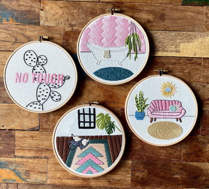 May include: Four embroidered hoops featuring different designs. The first hoop has a pink and white design with a bathtub and the text "No Touch". The second hoop has a pink and white design with a sofa and a plant. The third hoop has a green and white design with a window and a plant. The fourth hoop has a pink and white design with a cactus and the text "No Touch".