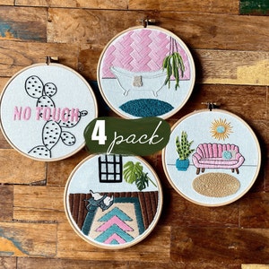 May include: Set of four embroidered hoop art pieces with various designs. The designs include a cactus with the text "No Touch", a bathtub with a plant, a sofa with a plant and a sun, and a rug with a plant and a window.