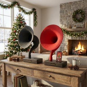 Puede incluir: Dos altavoces decorativos con forma de gramófono, uno negro y otro rojo, sobre una mesa de madera. Un smartphone muestra un gráfico de árbol de Navidad. La escena tiene un ambiente navideño con un árbol y una chimenea.