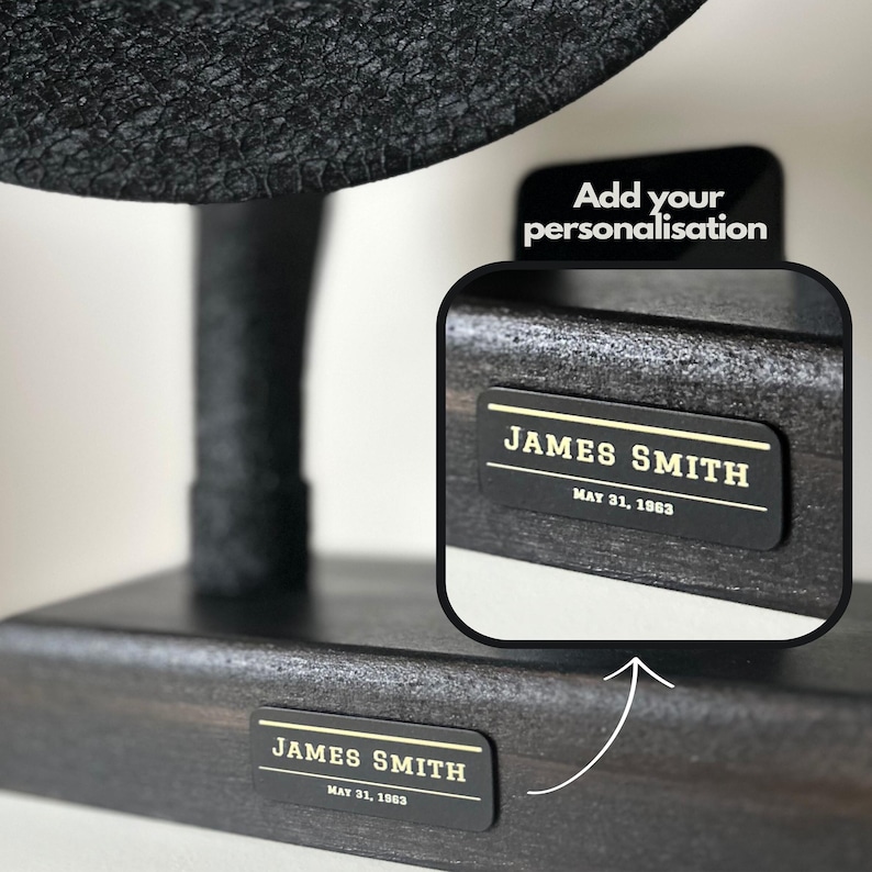 May include: Black wooden stand with a round black top. The stand has a personalised nameplate with the text "JAMES SMITH MAY 31, 1963".