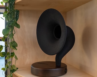 May include: A black vintage-style speaker with a large horn and a wooden base. The speaker is on a wooden shelf.