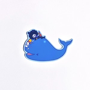 May include: A blue whale sticker with a black and white character riding on top. The character is wearing a red hat and holding a musical instrument.
