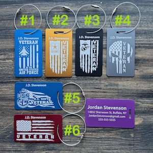 May include: Six different luggage tags with a veteran theme. The tags are made of metal and have a variety of designs, including the American flag, a skull, and a military emblem. Each tag has a different branch of the military represented, including the Air Force, Army, Marines, Navy, and a generic veteran tag. The tags are numbered 1 through 6.