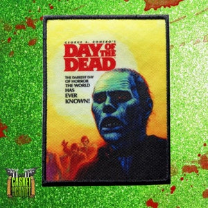 May include: A black and yellow embroidered patch with the text "George A. Romero's Day of the Dead" and a zombie with red eyes. The text below the title reads "The darkest day of horror the world has ever known!"