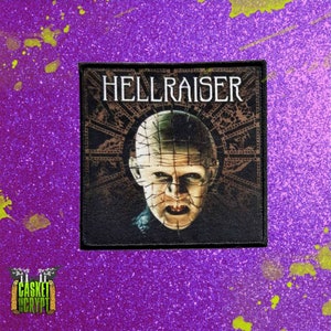 May include: A black and white embroidered patch with the text "HELLRAISER" in white lettering. The patch features a close-up of a character with a face covered in a grid of pins.