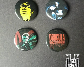 May include: Four round black button pins with different images. The first pin features a yellow and black image of a man's face. The second pin features a blue and black image of a man and woman. The third pin features a black and green image of a man's face. The fourth pin features a black and red image with the text "Dracula Prince of Darkness".