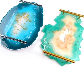 May include: Two decorative resin trays with metallic handles. One tray is teal and blue with silver handles, and the other is green and cream with gold handles. Both trays have gold flecks and a unique, organic shape.