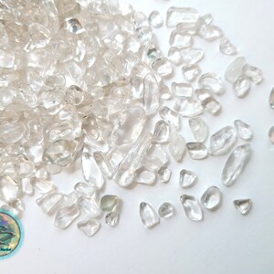 May include: A pile of clear quartz chips, scattered on a white background. The chips are various sizes and shapes, with some having a slight iridescent sheen.