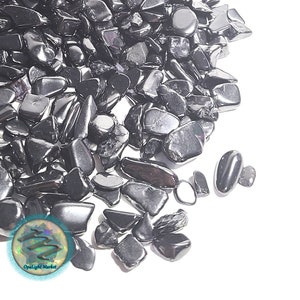 May include: A pile of black obsidian chips, a type of volcanic glass, on a white background. The chips are various sizes and shapes, with some having a shiny, metallic finish.