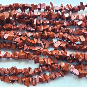 May include: A strand of red jasper chip beads. The beads are irregular in shape and have a natural, rough texture.