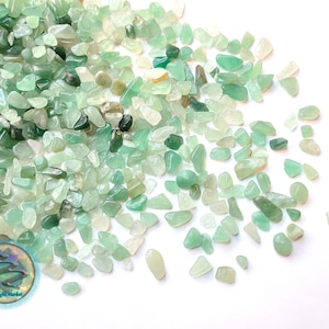 Peut inclure: Gros plan sur un tas de petites pierres de jade vertes et roulées. Les pierres sont de différentes nuances de vert, du clair au foncé. Les pierres sont éparpillées sur un fond blanc.