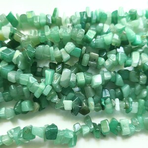 May include: A strand of light green jade chip beads. The beads are irregular in shape and size, with some being more rectangular and others more rounded. The beads are strung on a clear thread.