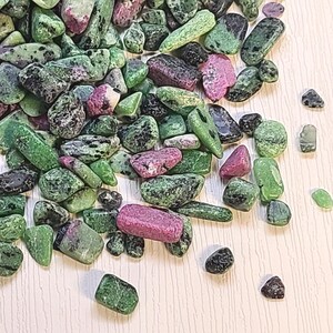 May include: A pile of green, pink, and black tumbled stones. The stones are smooth and have a variety of shapes and sizes.