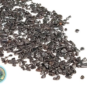 May include: A close-up of a pile of black hematite chips. The chips are small and irregular in shape, and they have a shiny, metallic finish.