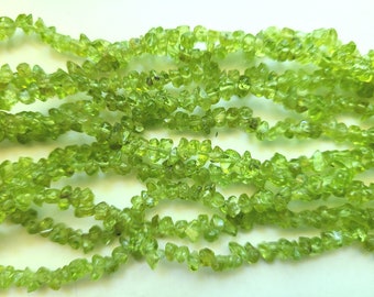 May include: A strand of green peridot chip beads. The beads are irregular in shape and have a natural, rough texture.