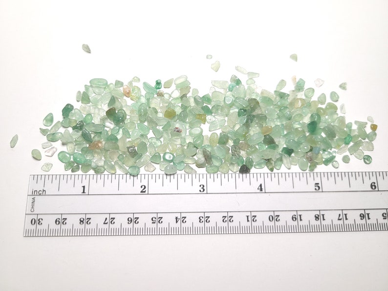 Puede incluir: Un mont&oacute;n de peque&ntilde;as piedras preciosas de aventurina verde pulidas. Las piedras son de varios tonos de verde, con algunas &aacute;reas transl&uacute;cidas. Una regla con medidas en pulgadas se coloca junto a las piedras preciosas.