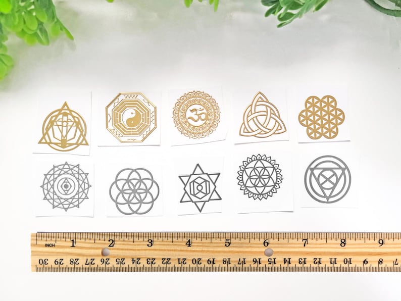 May include: Ten gold and silver temporary tattoos with geometric designs, including a flower of life, a yin yang symbol, and a Celtic knot. The tattoos are arranged in two rows of five on a white background.