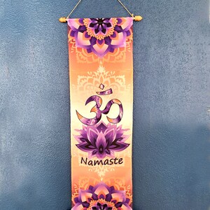 May include: A decorative wall hanging with a purple and orange mandala design. The hanging features the Om symbol and the word "Namaste" in a white font.