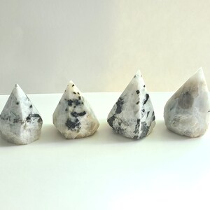 May include: Four white and black gemstone points, also known as rainbow moonstone points, arranged in a row on a white surface.