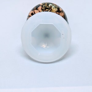 May include: A white resin cabochon with a clear, octagonal top and a brown and gold resin base.