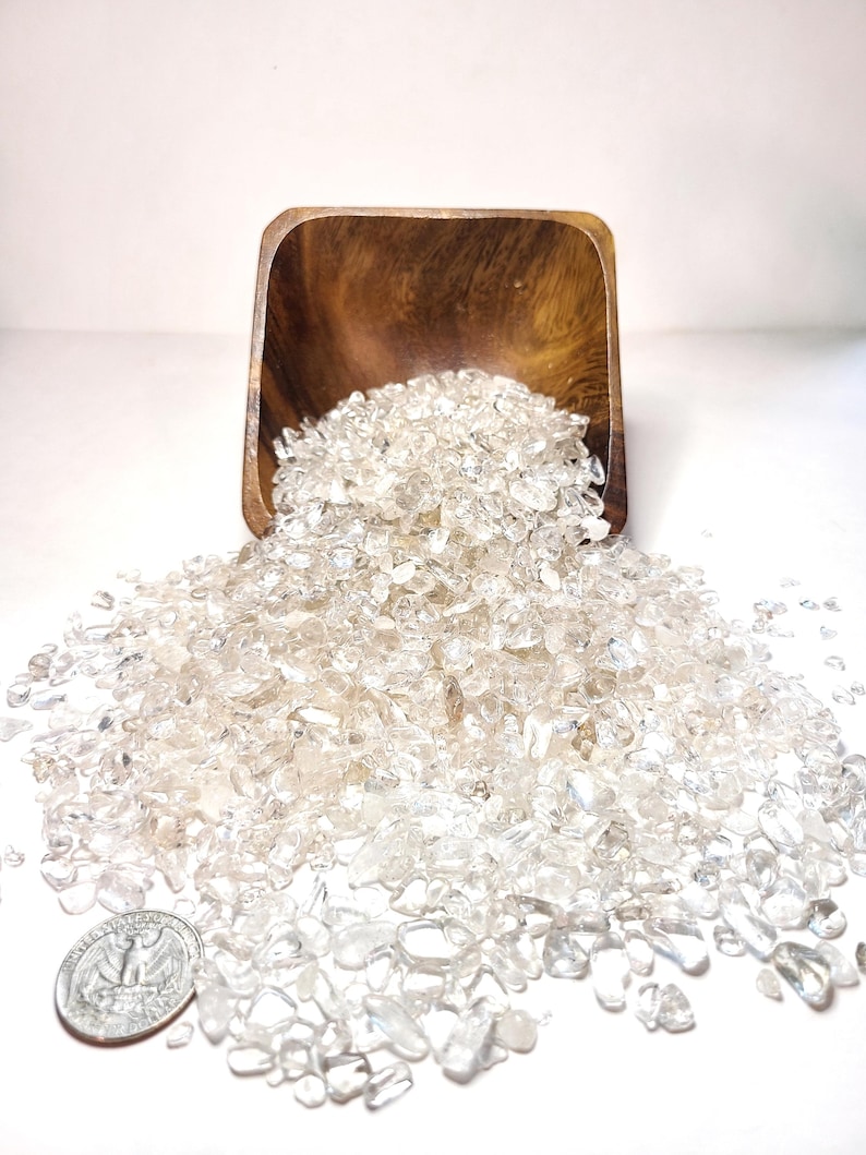 May include: A wooden bowl overflowing with clear quartz crystals, spilling onto a white surface. A US quarter is included for scale.