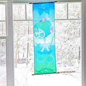 May include: A blue and green tapestry with a yin yang symbol and a meditating figure. The tapestry is hanging in a window with a snowy view outside.