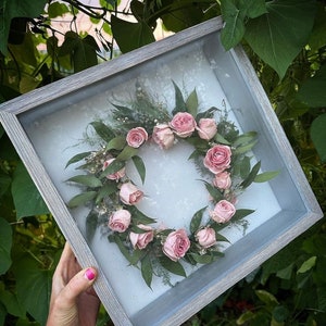 A gray wooden shadow box with a glass front containing a preserved bridal crown . Boutonnière, corsage etc. can also be preserved like this.