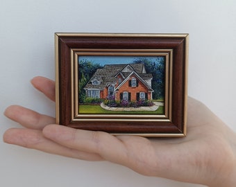 May include: A framed painting of a brick house with a green lawn and landscaping. The house has a white trim and a brown roof.