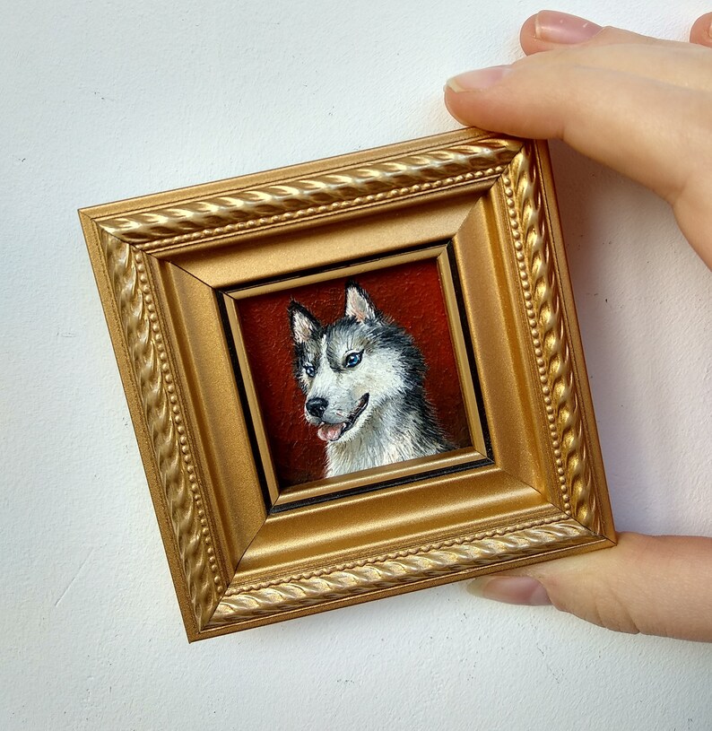 May include: A framed painting of a husky dog with blue eyes. The dog is painted in a realistic style with a white and gray coat. The frame is gold with a rope-like design.