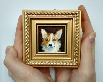 May include: A small, square, gold-framed painting of a Corgi dog. The dog has a white and orange coat, with a brown background. The frame has an ornate design.