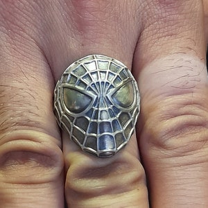 May include: A silver ring with a detailed design of a spider-man mask.