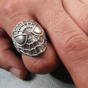 May include: A silver ring with a detailed design of Spider-Man's face and web.