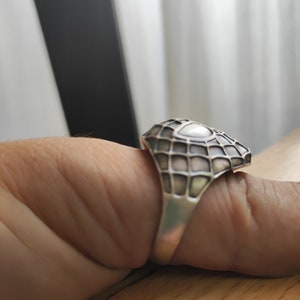 May include: A silver ring with a geometric design. The ring is worn on a finger.