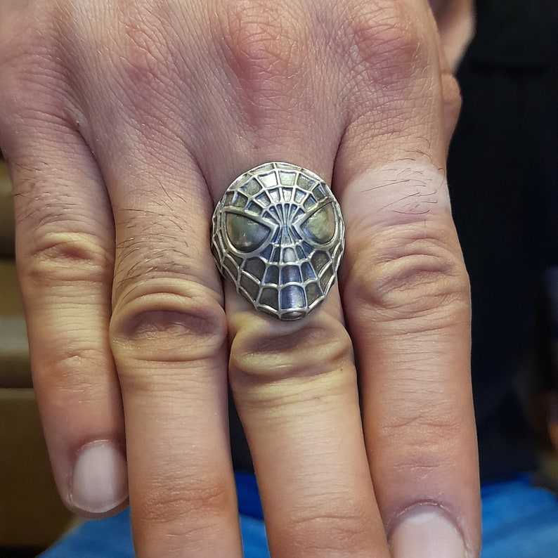May include: A silver ring with a detailed design of a spider-man mask.