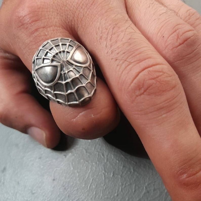 May include: A silver ring with a detailed design of Spider-Man's face and web.