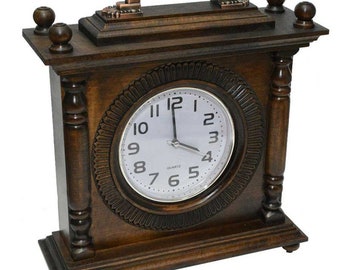 Può includere: Un orologio da camino in legno marrone scuro con un quadrante bianco. L'orologio ha una cornice circolare decorativa attorno al quadrante e una maniglia color rame sulla parte superiore. L'orologio è in stile classico e vintage.