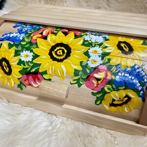 May include: A wooden bread bin with a hand-painted design of sunflowers, daisies, and other flowers in shades of yellow, red, blue, and green.