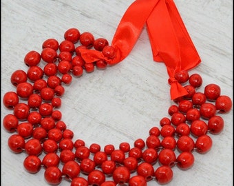 May include: A vibrant red beaded necklace with a cascading design. The necklace features numerous round, glossy red beads, strung together to create a layered effect. A bright red satin ribbon is used for the closure, adding a pop of color.