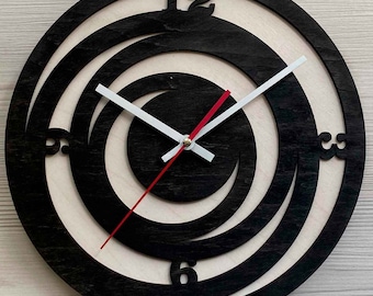 May include: A black and white wooden clock with a spiral design. The clock has a red hour hand and a white minute hand. The numbers 12, 3, 6, and 9 are visible on the clock face.