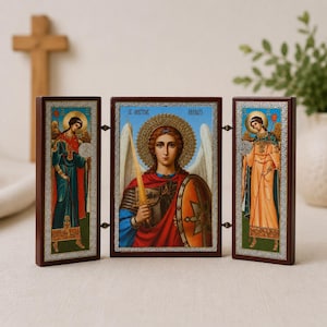 May include: A triptych icon featuring three panels with religious figures. The central panel depicts an angel with a sword and shield, while the two side panels show standing angels. Each panel has a dark wood frame with silver-toned borders.