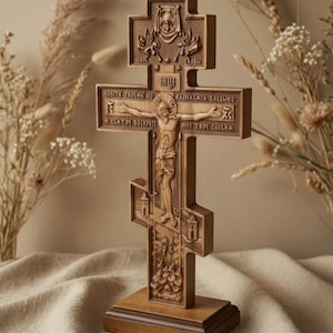 May include: A wooden Orthodox cross with intricate carvings. The cross features a depiction of Jesus Christ on the cross, with inscriptions in a foreign language. The cross is mounted on a rectangular base and is a religious item.